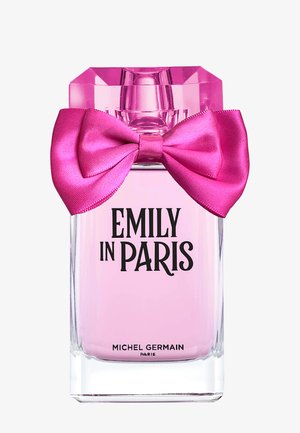 Flacon de parfum en verre transparent avec un liquide rose, un nœud en satin rose vif, étiqueté Emily in Paris par Michel Germain Paris.