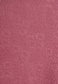 Tissu texturé d'une couleur rose douce présentant des motifs floraux et des coutures délicates, créant une apparence dimensionnelle.