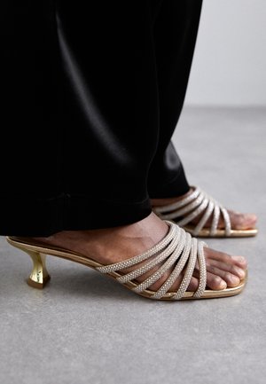 Gullige sandaler med stropper og en kort, utsvingt hæl. Stroppene er prydet med små, klare rhinestones for ekstra detaljer.