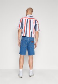 Krátký rukáv, pruhované tričko v červené, modré a bílé barvě, skvělě se hodící k modrým denimovým šortkám. Viditelné zadní kapsy a hnědá cedulka na šortkách.