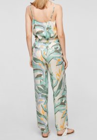Květinový overal se světle zeleným, žlutým a modrým vzorem, který má volný střih, tenké ramínka a elastický pas.