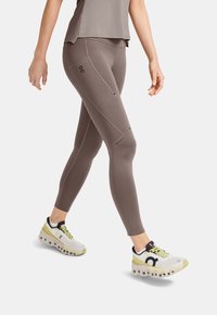 Ljusbruna leggings i stretchmaterial, med en åtsittande design och sömdetaljer, i kombination med vita sneakers med gröna accenter.