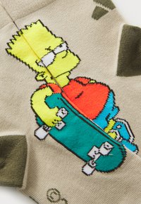 Bežové ponožky s karikatúrou postavy na skateboarde, so zelenými akcentmi a štruktúrovaným pleteným dizajnom.
