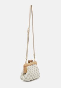 Small beige crossbody bag with polka dots, wooden frame, round wooden clasp, and adjustable leather strap.