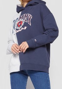 Sudadera con capucha de diseño en bloques de color; secciones gris y azul marino. Presenta gráficos de logo en el pecho y puños acanalados.