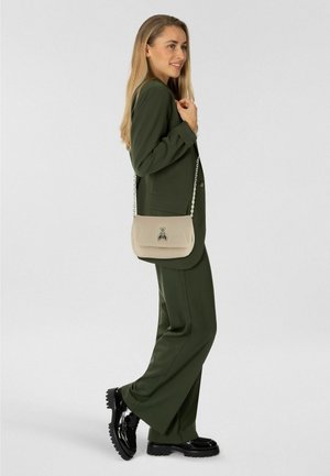 Grüner, maßgeschneiderter Anzug mit einer hellbeigen Schultertasche mit dekorativem Verschluss und schwarzen, klobigen Lacklederschuhen.