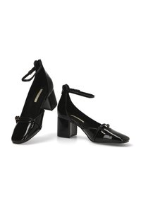 Zapatos de tacón cuadrado de charol negro con correa en el tobillo, punta afilada y detalle de lazo frontal. Textura lisa y acabado brillante.