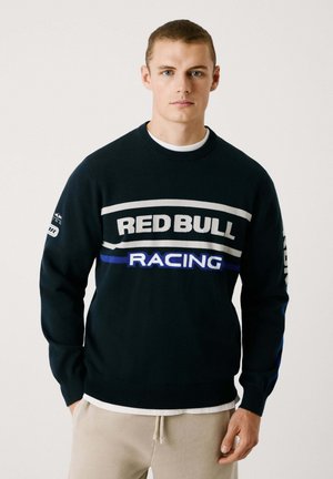 Sweatshirt navy avec le texte "RED BULL RACING" en blanc et rayures bleues. Dispose de poignets et d'ourlet côtelés, d'un tissu lisse et d'un col rond.