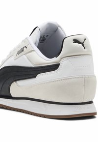Puma-tossut valkoisella päällä, mustilla nahkakoristeluilla, pehmeällä mokka kantapäällä, teksturoitua verkkokangasta olevalla kielillä ja ruskealla kumipohjalla.