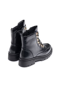 Botas de cuero negro con puntera redonda, cordones en el frente, ojales dorados y una suela de goma gruesa. Cuentan con una cremallera lateral para facilitar su uso.