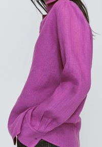 Lavender linen long-sleeve shirt with a button collar, relaxed fit, and visible seam details. Features a single button at the cuff.