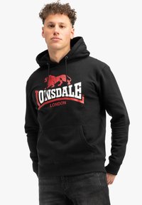 Sudadera negra con capucha y cordón, que presenta un gran gráfico de un león rojo y el texto "LONSDALE LONDON". Bolsillo frontal tipo canguro y puños acanalados.