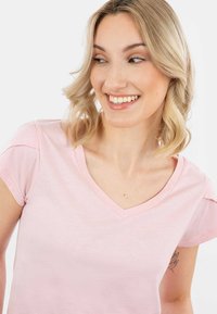Šviesiai rožinė, trumpa rankovė viršūnė su V formos iškirpte, pagaminta iš minkštos medžiagos. Pasižymi subtiliais peties akcentais, lygiu tekstūru ir laisvu siluetu.
