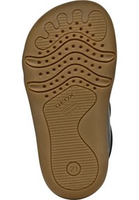 Brun gummisula med ett vågigt mönster och flera små cirkulära utskärningar. "GEOX ITALIENSK PATENT" präglat på ytan.