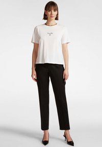 T-shirt bianca a maniche corte con scollatura rotonda, caratterizzata dalla scritta nera "Dragonfly" e da una grafica a stella, abbinata a pantaloni neri su misura.