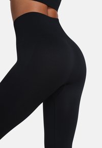 Čierne legíny s vysokým pásom vyrobené z elastickej, textúrovanej látky. Majú bezšvovú konštrukciu a priliehavý strih cez nohy.