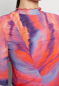 Flerfärgad blus med veckad design i orange, lila och blå nyanser. Texturerad tyg med en volangkrage.