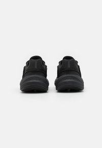 Zapatillas negras con parte superior de tela suave y suela acolchada, que cuentan con elementos de diseño minimalistas y una marca en el talón.