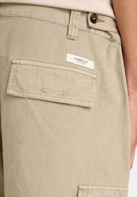Beige cargoshorts van een textuurstof. Heeft een achterzak met klep en het label "ELEMENT CO. SINCE 1992" erop gestikt.