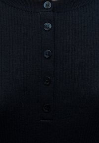 Gros plan d’un vêtement en tricot côtelé noir avec six boutons noirs à quatre trous disposés verticalement au centre.