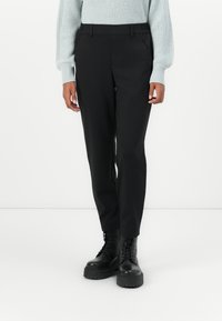 Zwarte broek met een strak ontwerp, met zijzakken en een gladde, textuurstof. G gedragen met zwarte veterschoenen en een lichte trui.