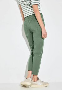 Groene katoenen broek in een gemêleerde stof met een smal toelopende pasvorm, voorzien van achterzakken en een cropped lengte. Gecombineerd met beige sneakers.