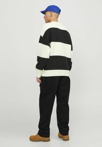 Maglione a righe bianche e nere con vestibilità rilassata, scollo rotondo, tessuto leggero e polsini a costine, abbinato a pantaloni neri e stivali color sabbia.