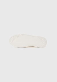 Suela de una zapatilla blanca que muestra detallados patrones en espiga y geométricos sobre un fondo blanco liso.
