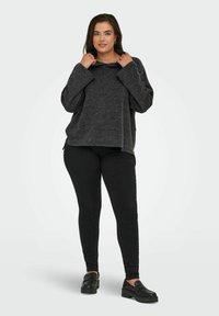 Tmav gray oversize pulover s kapucňou, rebrovanou textúrou a širokými rukávmi, skombinovaný s čiernymi priliehavými nohavicami a robustnými čiernymi topánkami.