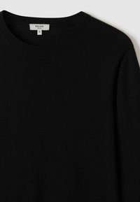 Pulover din lână neagră cu guler rotund, având un design simplu și minimalist. Eticheta indică mărimea M.