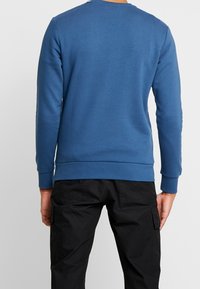 Sudadera azul hecha de una tela suave, con cuello redondo y puños acanalados, combinada con pantalones cargo negros con bolsillos laterales.