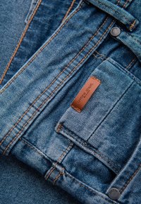 Ljusblå denimjeans med kontrasterande orangea sömmar, utrustade med en läderetikett, metallknapp och flera fickor.