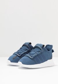 Zapatillas de malla azul con tres rayas azul marino, suela de goma y parte superior texturizada. Incluye diseño con cordones y bucle en la parte trasera.
