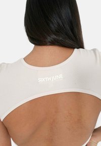 Top rigato beige chiaro con schiena scoperta, caratterizzato da un logo bianco "SIXTH JUNE" sotto il collo, che mette in evidenza il tessuto testurizzato e un design elegante.