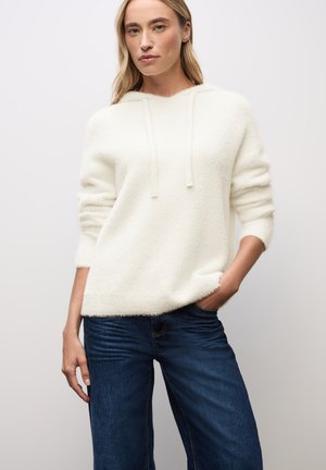 Krämfärgad, mjuk stickad tröja med huva, med en avslappnad passform och uppvikta ärmslut, tillsammans med mörkblå jeans.