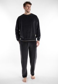 Zwart pyjama-set gemaakt van zachte stof; lange mouwen top met een ronde hals en bijpassende drawstring broek met een subtiele beige accent bij de taille.
