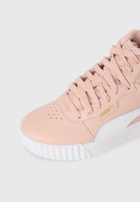 Světle růžová sneaker od Pumy s tlustou bílou podrážkou, strukturovanými tkaničkami, perforovanou špičkou a měkkým polstrováním viditelným na límci kotníku.