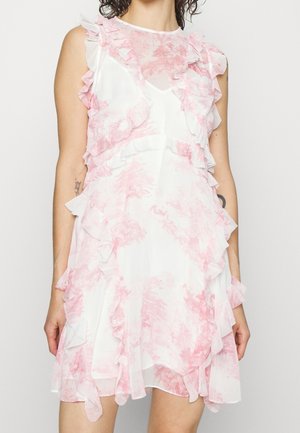 Mouwloze witte jurk met roze bloemmotief en gerimpelde rand, gedragen door een persoon met zichtbare armtatoeages.