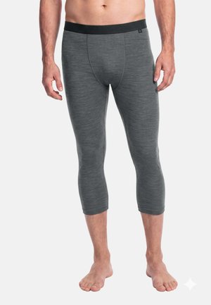 Personne torse nu portant des leggings gris ajustés trois-quarts avec une ceinture noire, debout pieds nus sur un fond blanc.