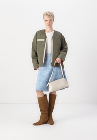 Olive green quilted bomber jacket, white top, light blue floral denim skirt, beige purse, and brown knee-high heeled boots.