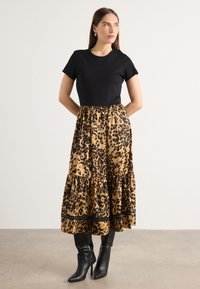 Top corto nero a maniche corte abbinato a una gonna a strati con stampa leopardata beige e nera. La modella indossa stivali neri a punta con un design a cono.