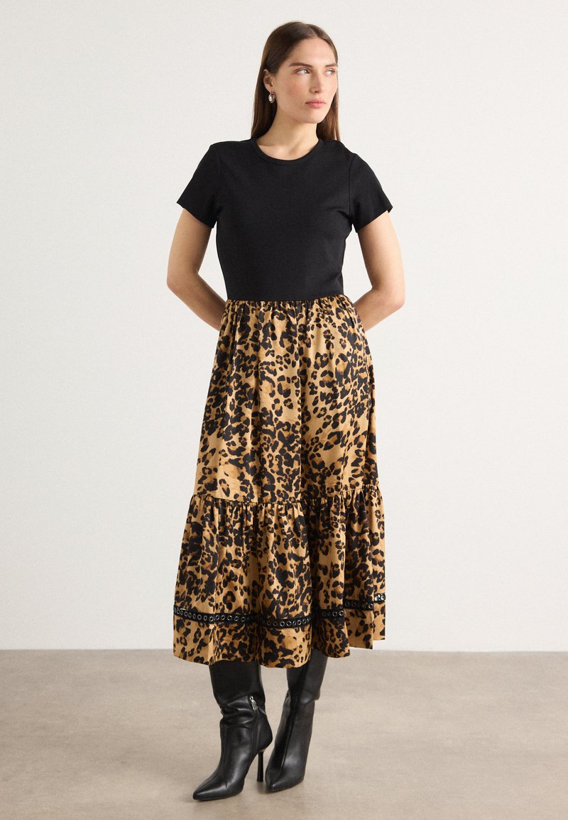 Top corto nero a maniche corte abbinato a una gonna a strati con stampa leopardata beige e nera. La modella indossa stivali neri a punta con un design a cono.