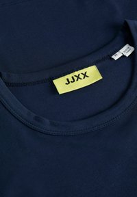 Námořnická modrá tričko z měkké látky s kulatým výstřihem, krátkými rukávy a výraznou žlutou etiketou s nápisem "JJXX" na krku.