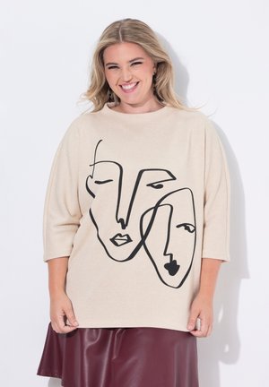 Maglione oversize beige con un disegno di linee nere che raffigura due volti astratti. Realizzato in un materiale morbido con maniche a tre quarti.