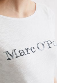 Hvid t-shirt med mærkenavnet "Marc O'Polo" i sort slidt tryk. Letvægts, blødt stof med rund halsudskæring og glat tekstur.