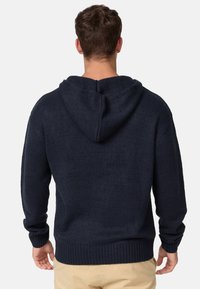 Haut à capuche tricoté bleu marine avec une surface texturée, doté d'une capuche à cordon de serrage et de poignets et d'un ourlet côtelés. La vue de dos montre une coupe décontractée.