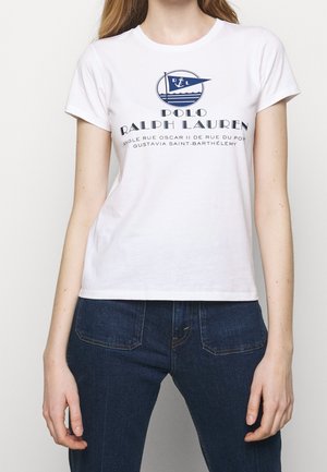 Kvinde iført en hvid Polo Ralph Lauren T-shirt med et blåt nautisk logo og mørkeblå jeans, vist fra nakke til hofter.