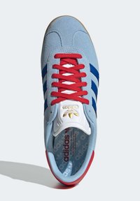 Baskets en daim bleu avec lacets rouges, ornées de trois rayures bleues, d'une languette blanche avec un logo doré, et d'une semelle en caoutchouc avec des accents rouges.