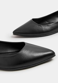 Bailarinas negras de punta afilada hechas de cuero suave, con un escote bajo en el empeine y suela de goma flexible, presentando un diseño sencillo y sin adornos visibles.