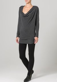 Grijze, lange mouw top met een gedrapeerde halslijn en textuurstof, gecombineerd met zwarte leggings en enkellaarzen met een gouden ritsdetail.